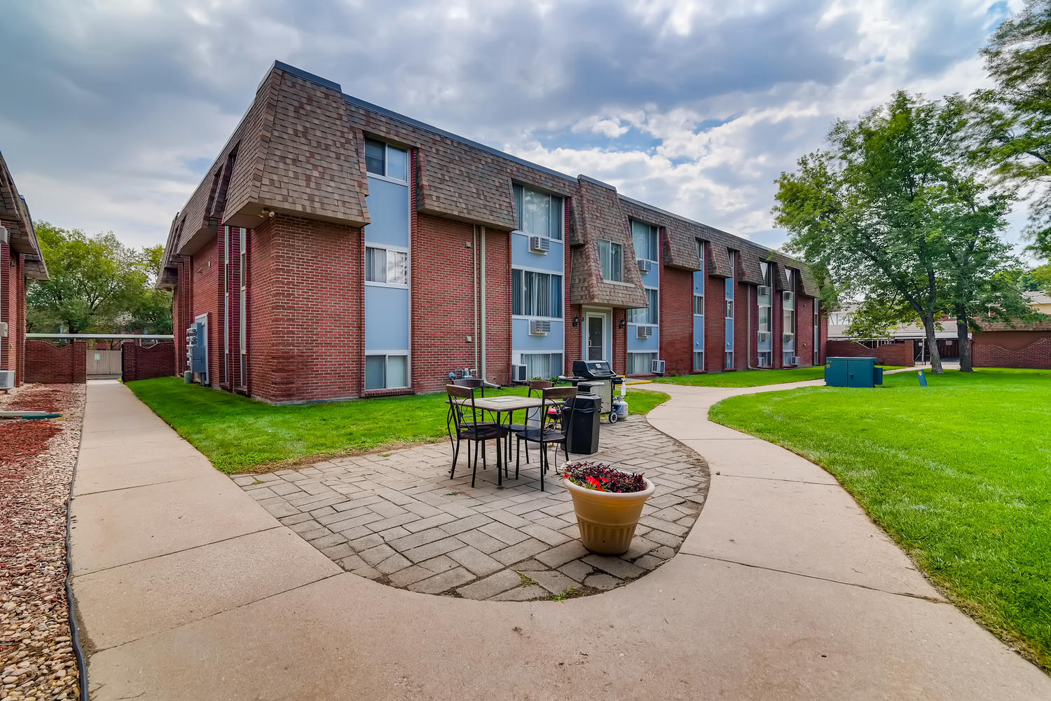 Brick and siding building exterior with picnic table, planter, and sidewalk.