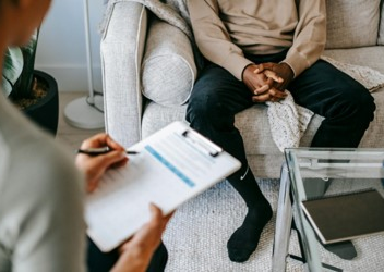 A professional with a clipboard interviewing a client sitting on a couch.