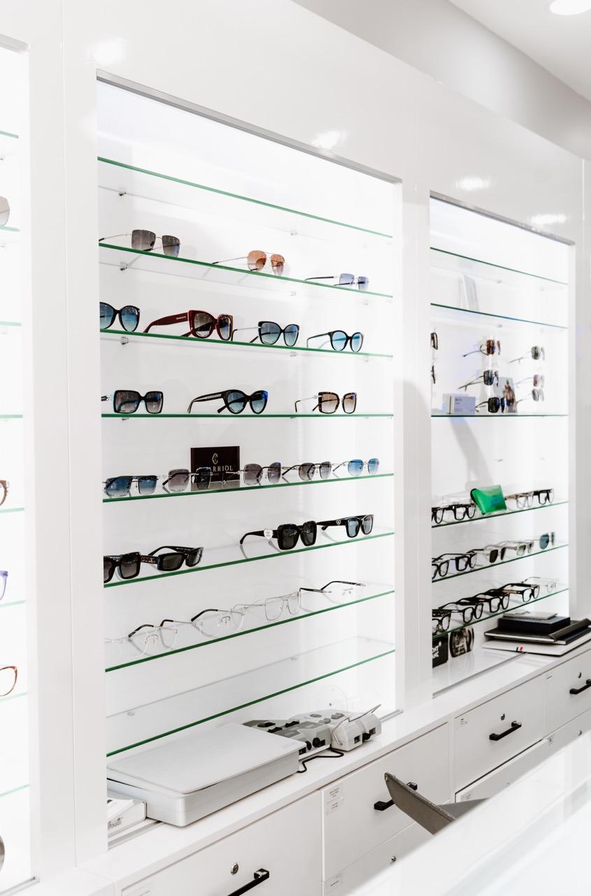 Designer sunglasses and prescription eyeglasses arranged on illuminated display shelves at TK Optome 