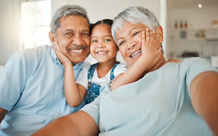 Grandparents posing with their grandchild who's lovingly sandwiched between them.