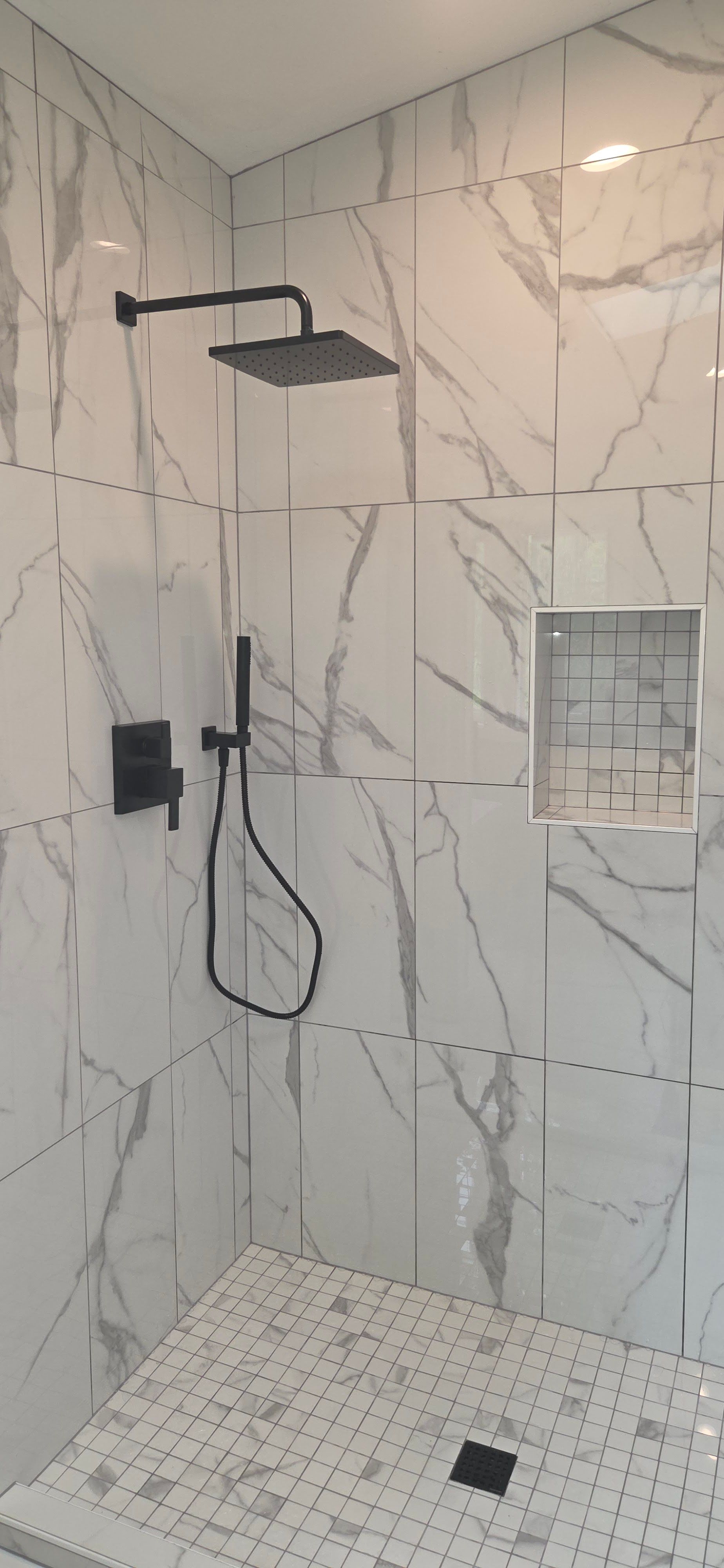 Modern walk-in shower featuring marble-style wall tiles, black rainfall showerhead, handheld shower  