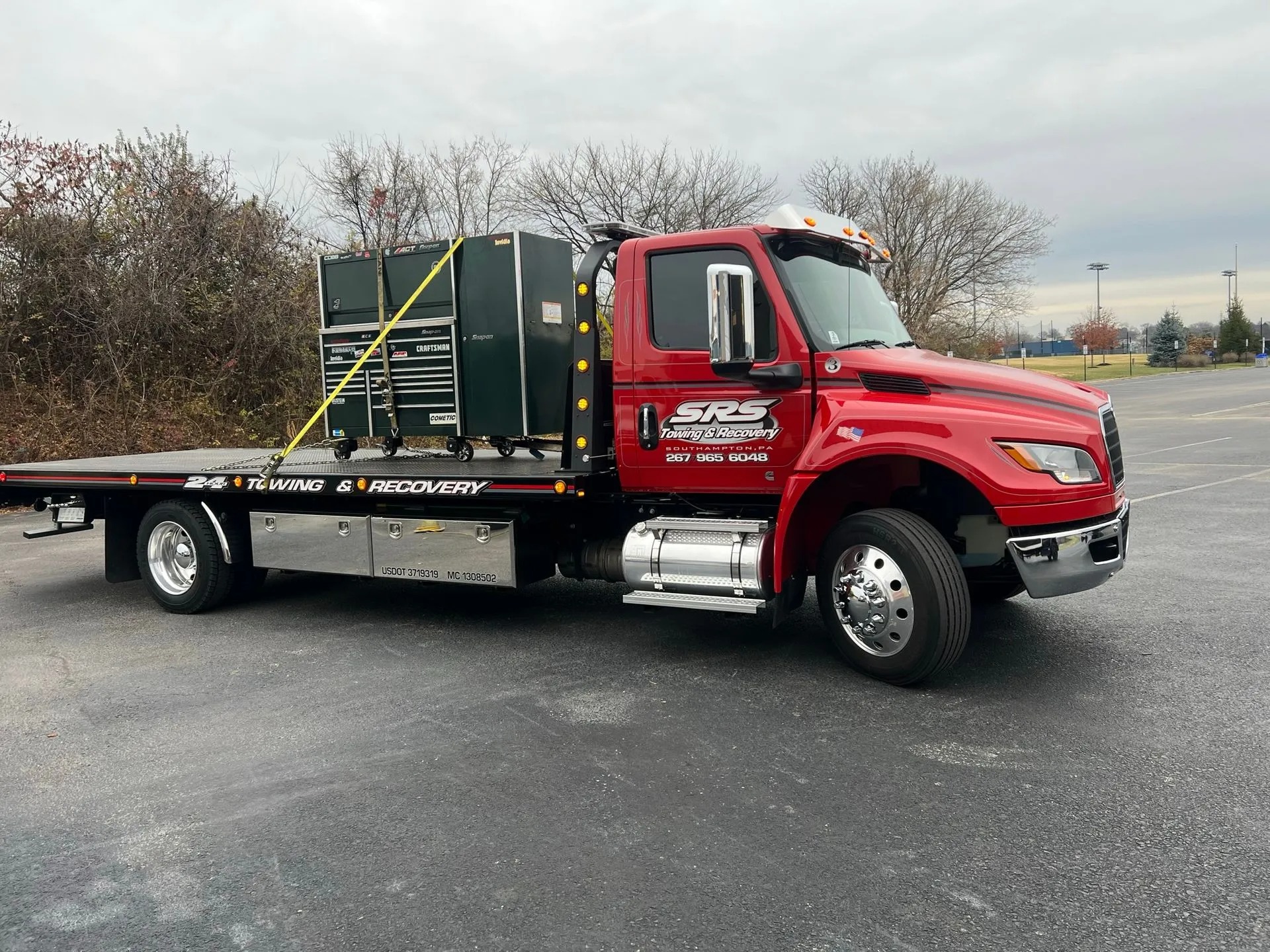 SRS Towing & Recovery’s red flatbed tow truck carrying a black tool chest with multiple drawers, secured with straps outdoors.