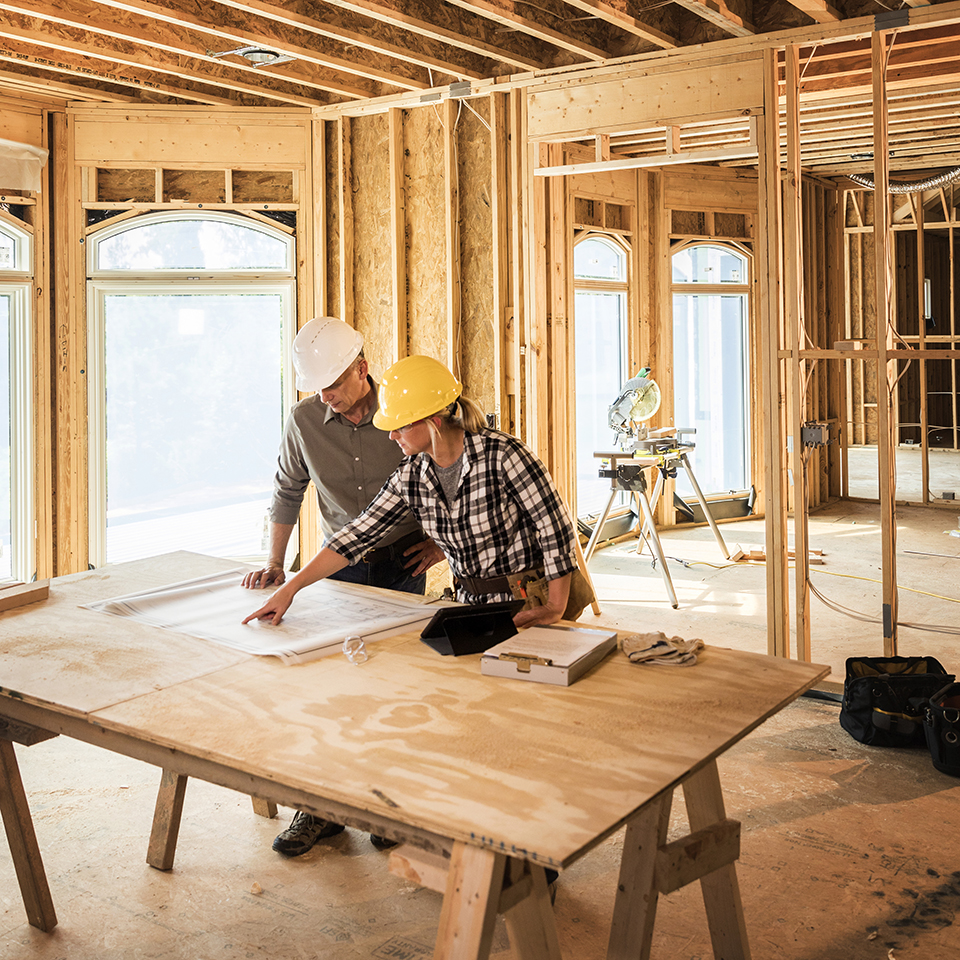 Two people looking at blueprints in a house under construction