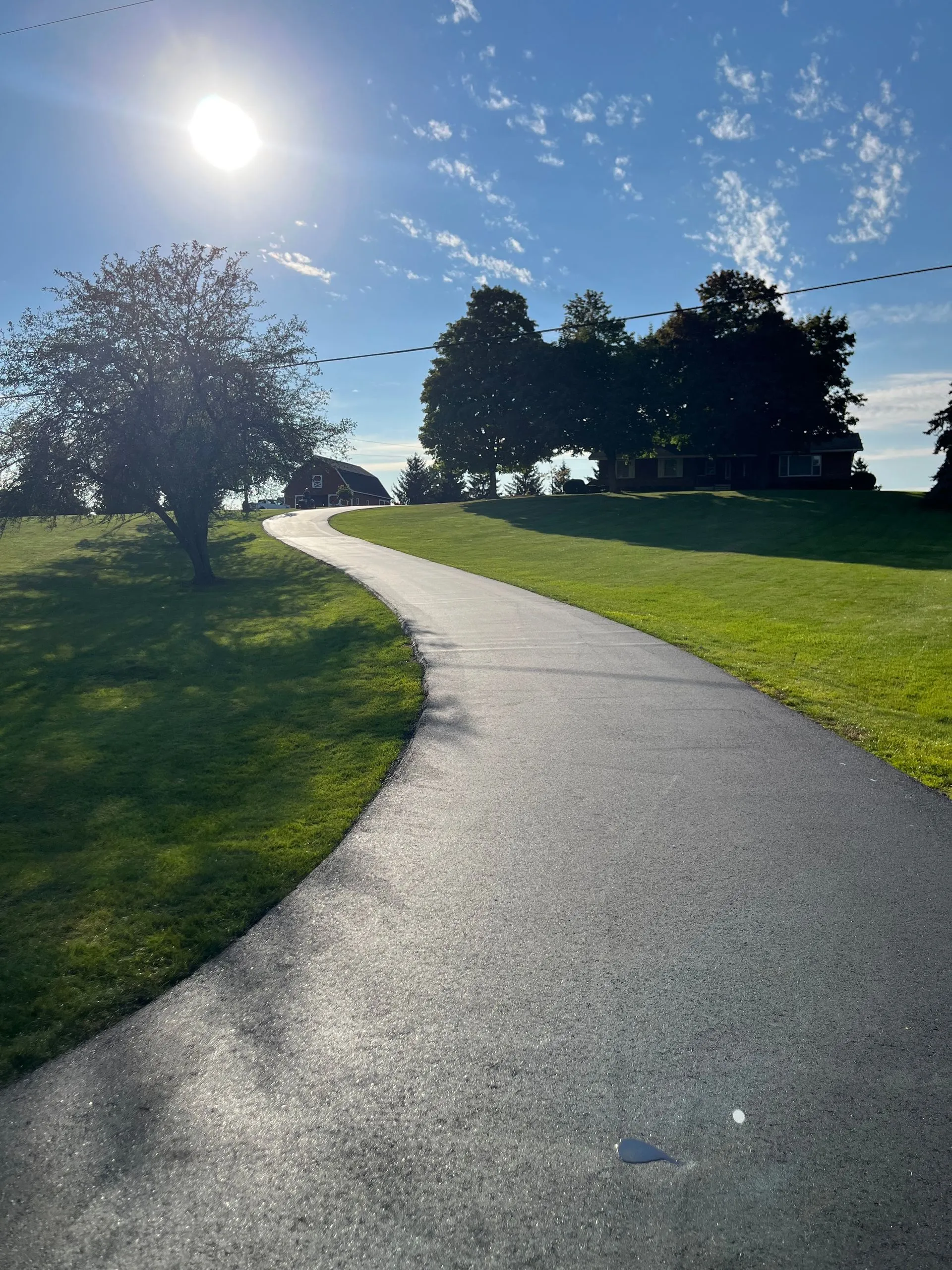 Newly paved winding driveway across open grassy terrain providing durable access to a countryside residential property.