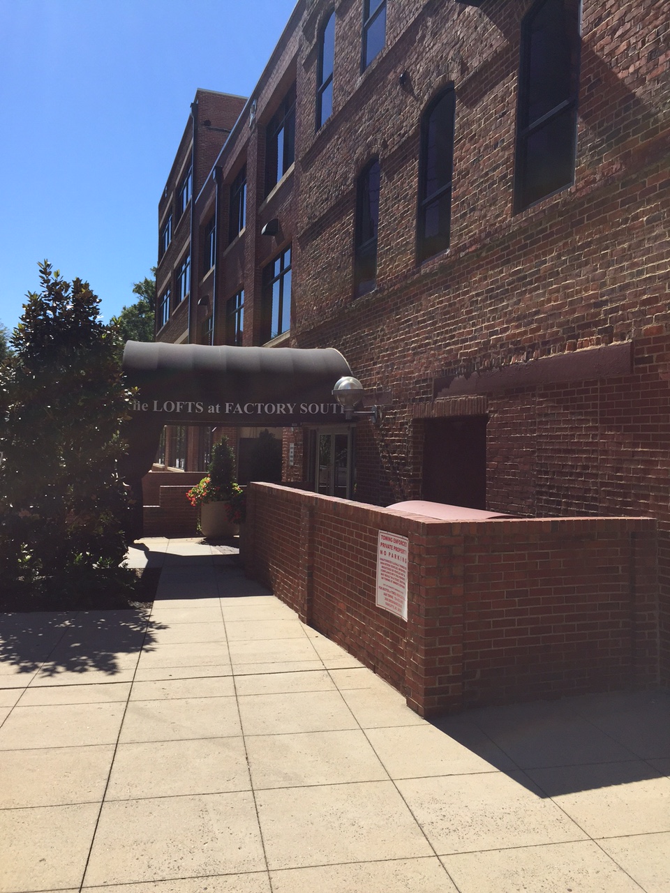 A brick building with a dark awning that reads "The Lofts at Factory South" is visible on a sunny day.