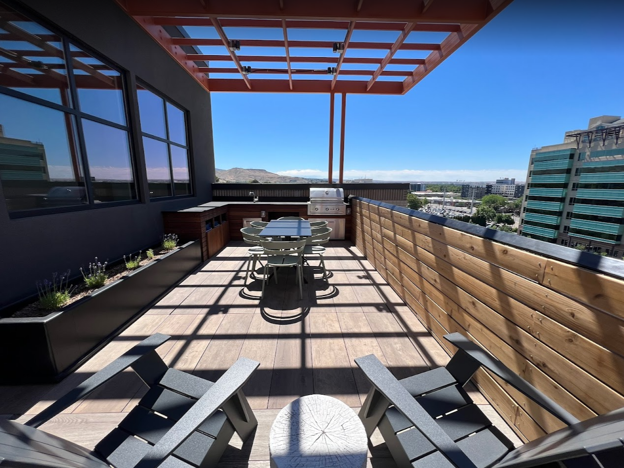 Chic rooftop lounge area with two black lounge chairs and bleached-wood stump-style side table in between with a view of the resident barbeque area and the Boise foothills