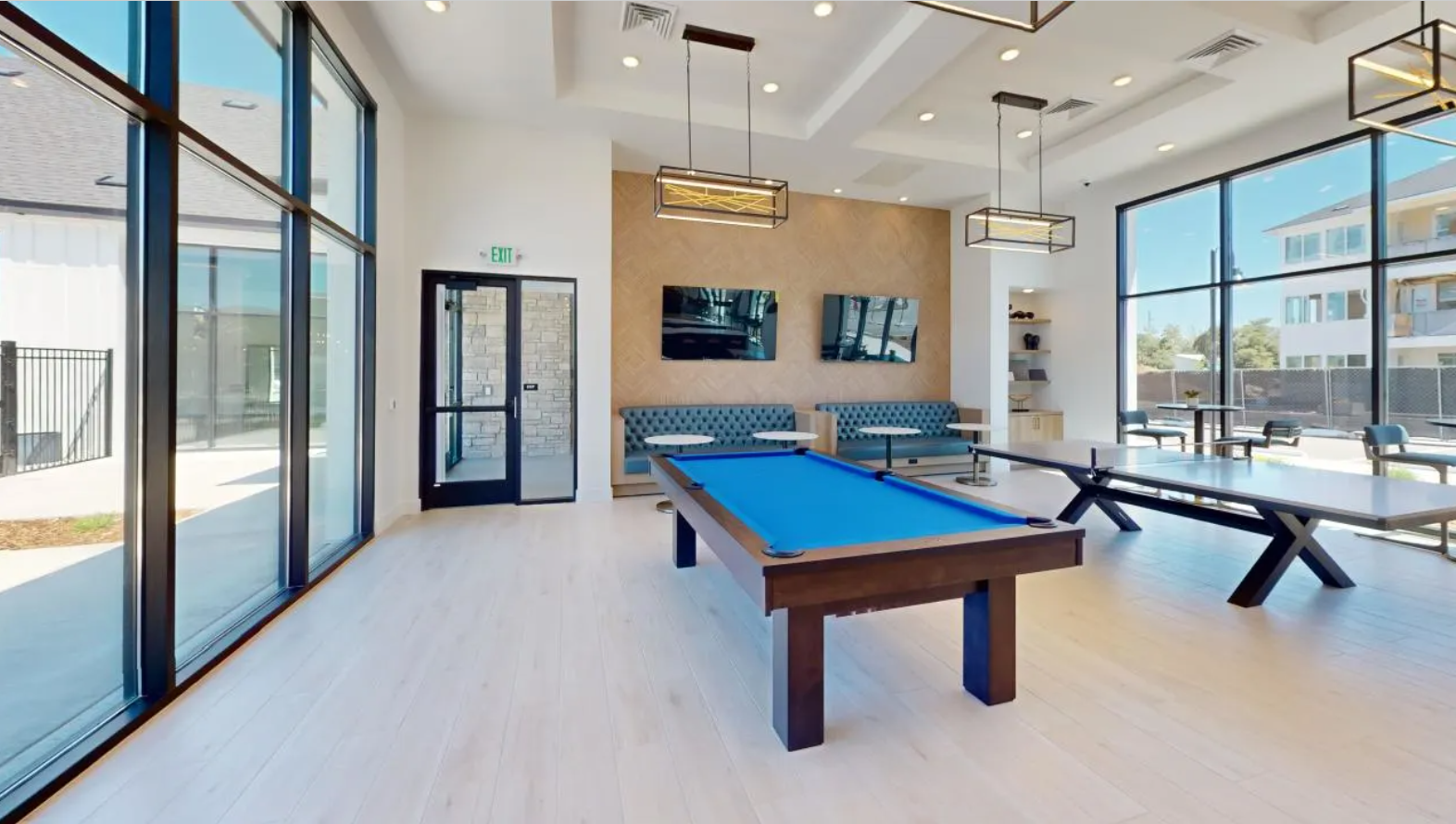 a game room with a pool and ping pong tables with booth seating and large windows