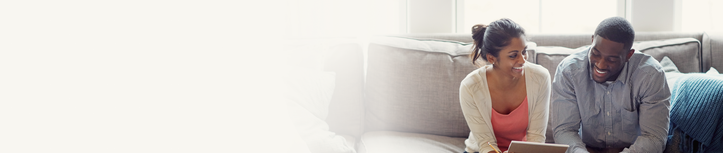 A smiling young couple sitting on their couch reviewing documents together.