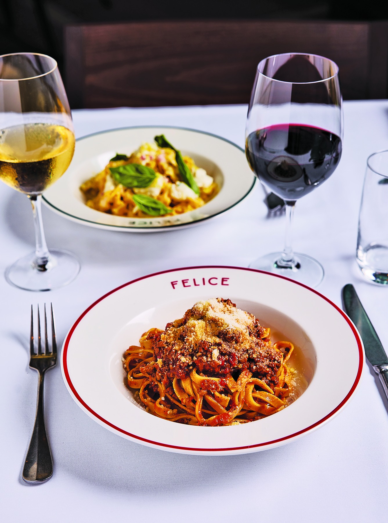 Classic Italian meat sauce over fresh pasta, served alongside a glass of red wine and a glass of white wine in a bright dining room.