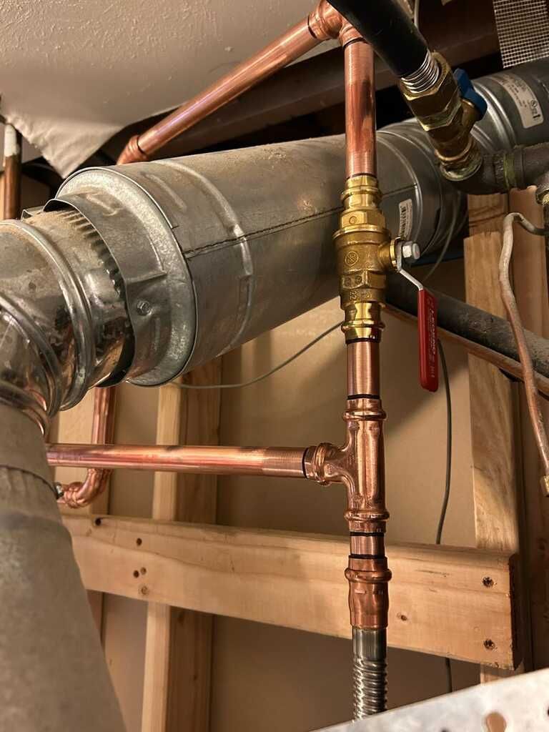 Close view of newly installed copper plumbing lines, fittings, shutoff valve, and connections beside 