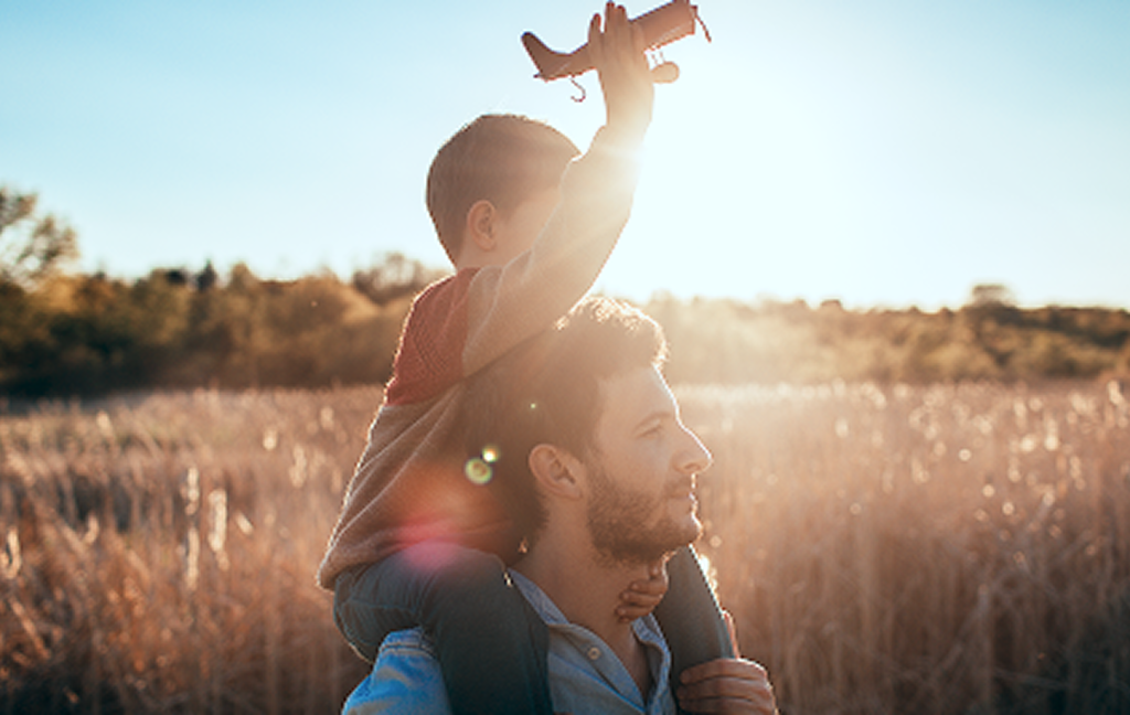Son holding toy airplane on his dad's shoulders.