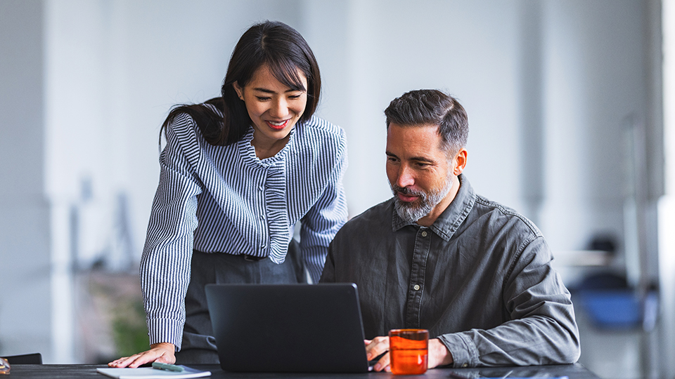 A woman and man in professional attire looking at a laptop.