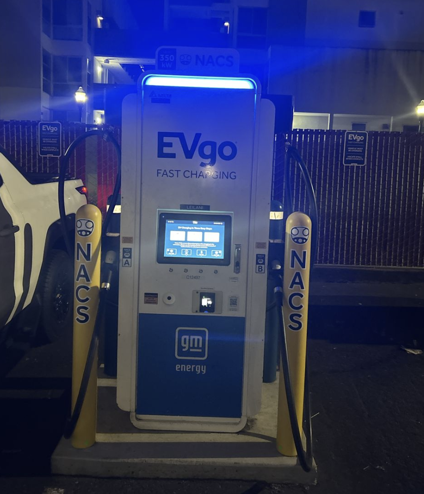 NACS EVgo fast charging unit installed in marked parking space at a public charging station, with EVgo logos on the charger, and yellow protective bollards around the unit.