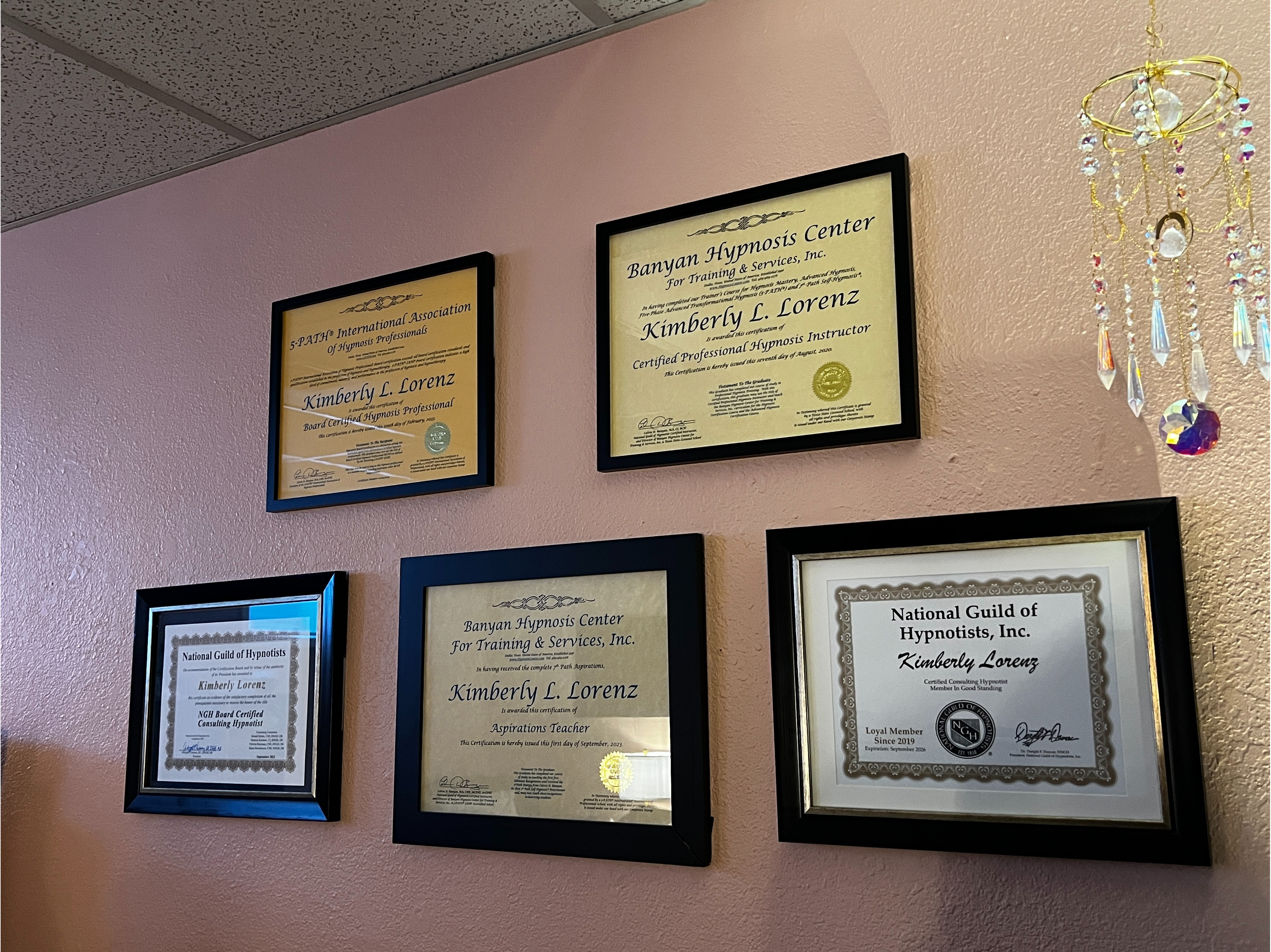 Certifications & Credentials Wall:  Professional certifications and hypnosis credentials displayed inside Lynne Coaching & Hypnosis, including board certification and advanced hypnosis training credentials demonstrating professional expertise and continuing education.
