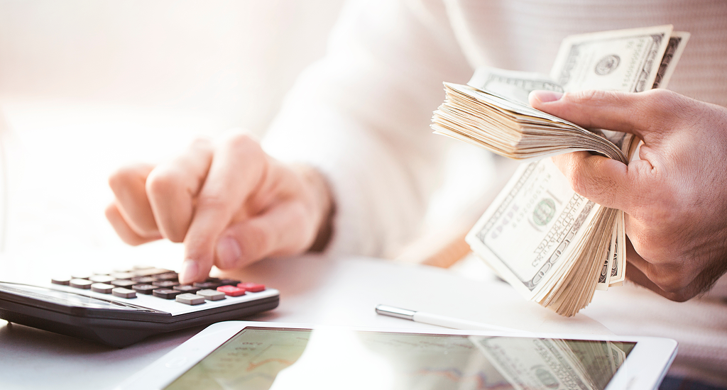Someone holding money and typing on a calculator.