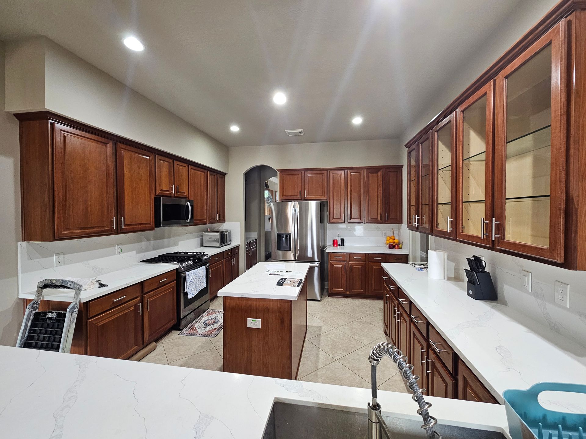 Elegant kitchen showcasing beautifully refinished dark wood cabinets, bright quartz countertops, stainless steel appliances, recessed lighting, and a spacious layout demonstrating premium cabinet painting and finishing craftsmanship.