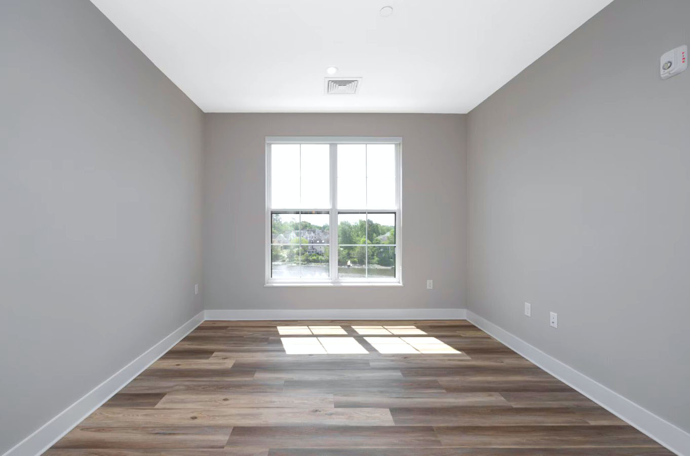A bright, minimalist bedroom at Creekline at Fairfield features wide-plank flooring and a large window with a scenic view.