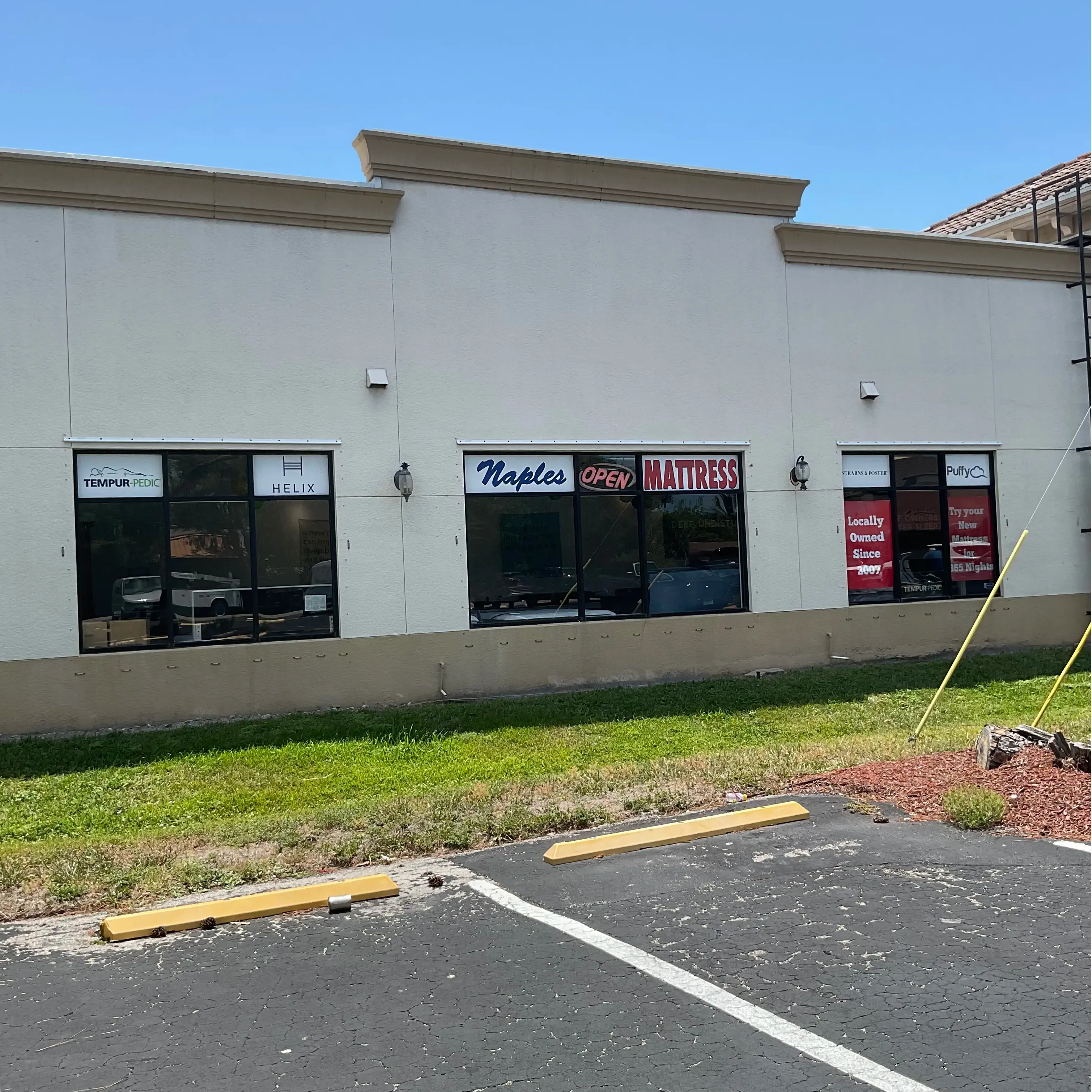 Rear exterior of Naples Mattress North, showing branded windows and nearby parking spaces.