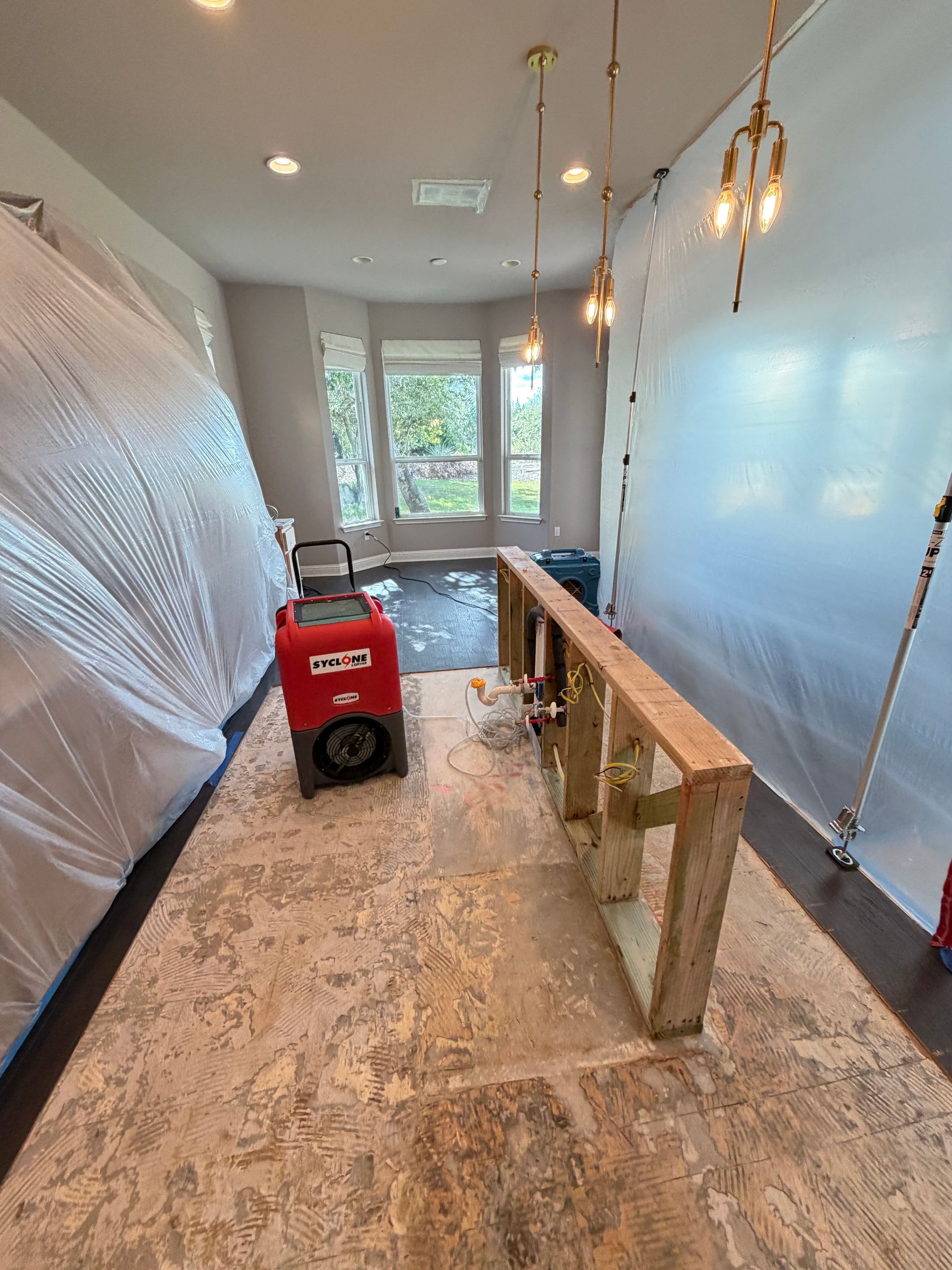 A large residential room undergoing restoration features removed flooring, exposed wall framing, pla 