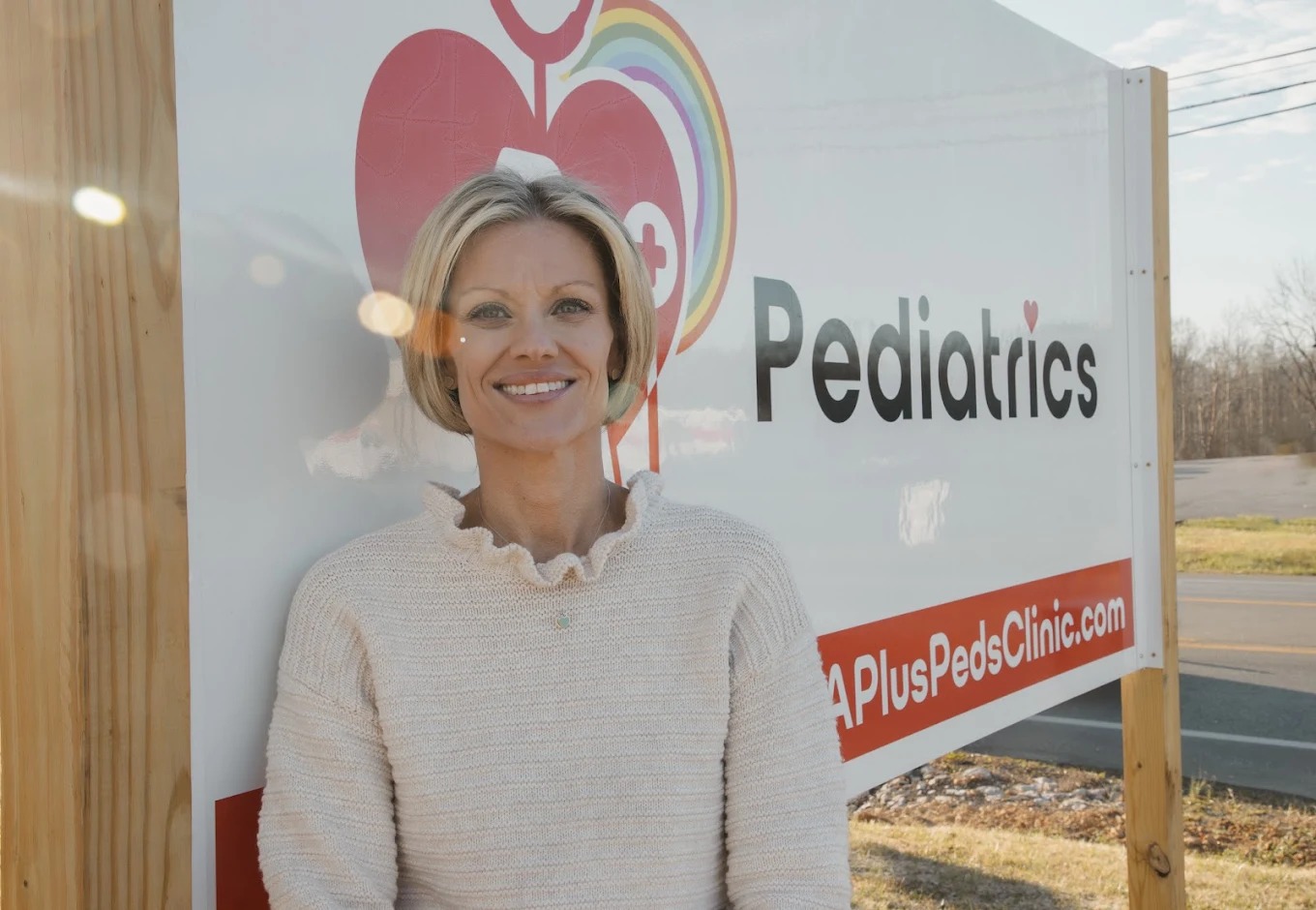 Jennifer Maupin standing beside the A+ Pediatrics outdoor sign in Irvine, Kentucky.