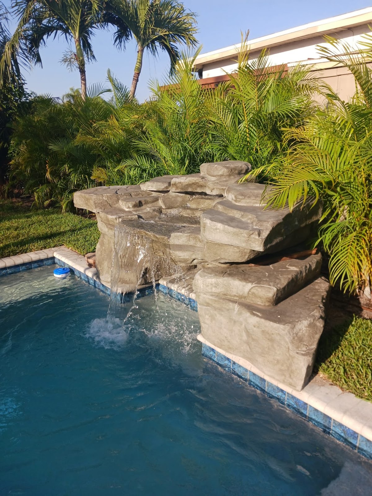Custom swimming pool with a natural stone waterfall feature, tropical landscaping, and resort-style backyard design.