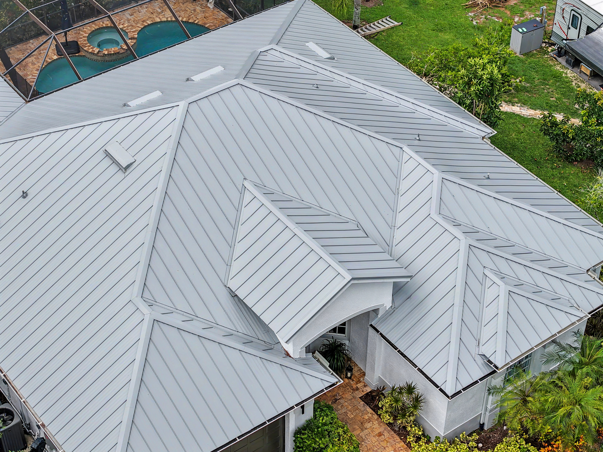 Close drone view of a light gray standing seam metal roof highlighting its intersecting roof section 