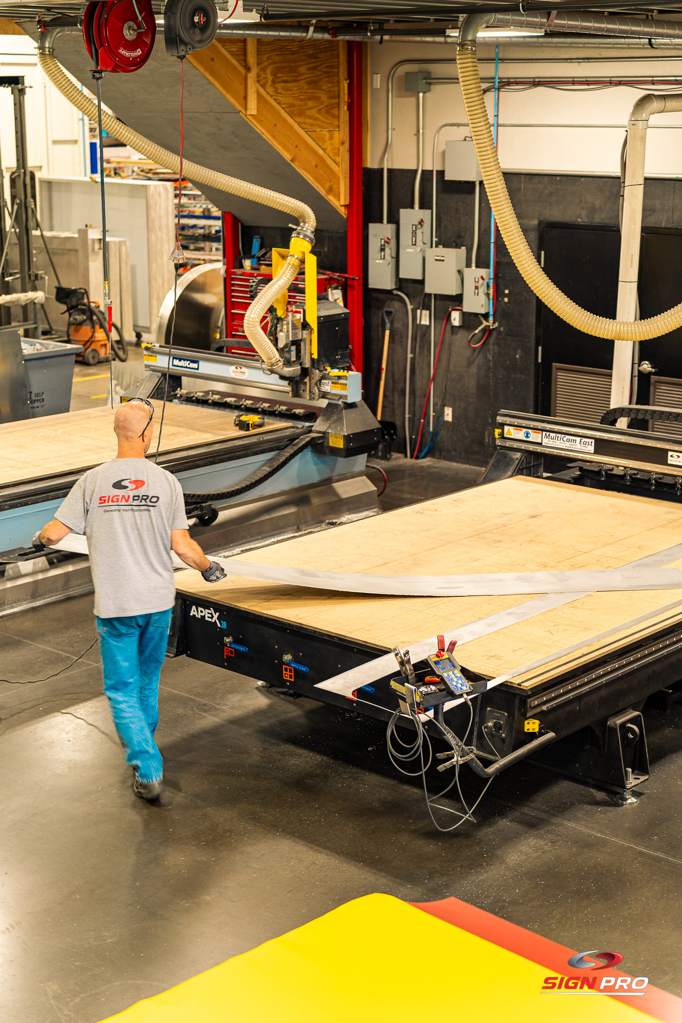A Sign Pro team member operates a MultiCam CNC router in the fabrication shop, cutting large signage materials with precision and efficiency for custom sign production.