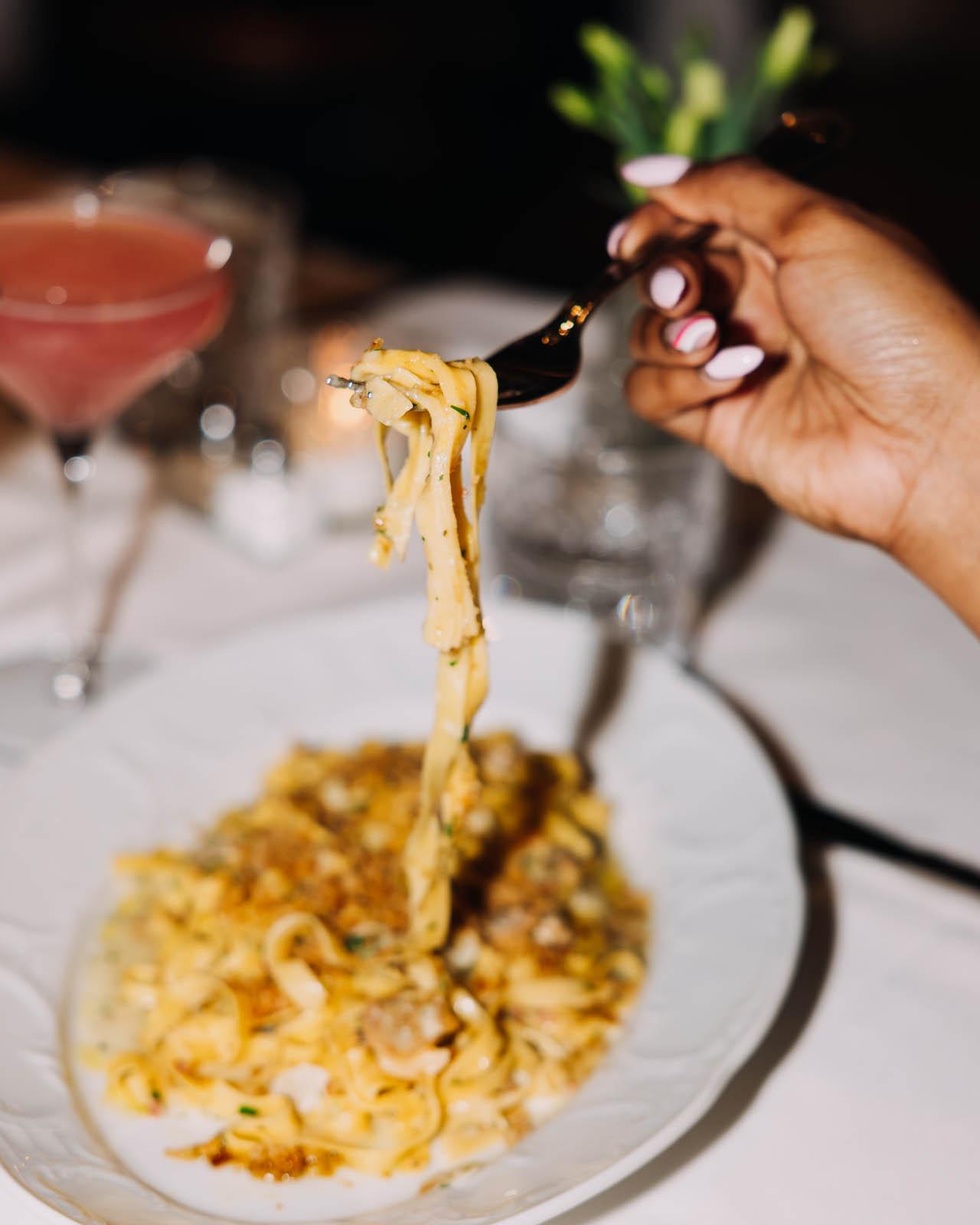 Woman's hand pulling up pasta from her plate
