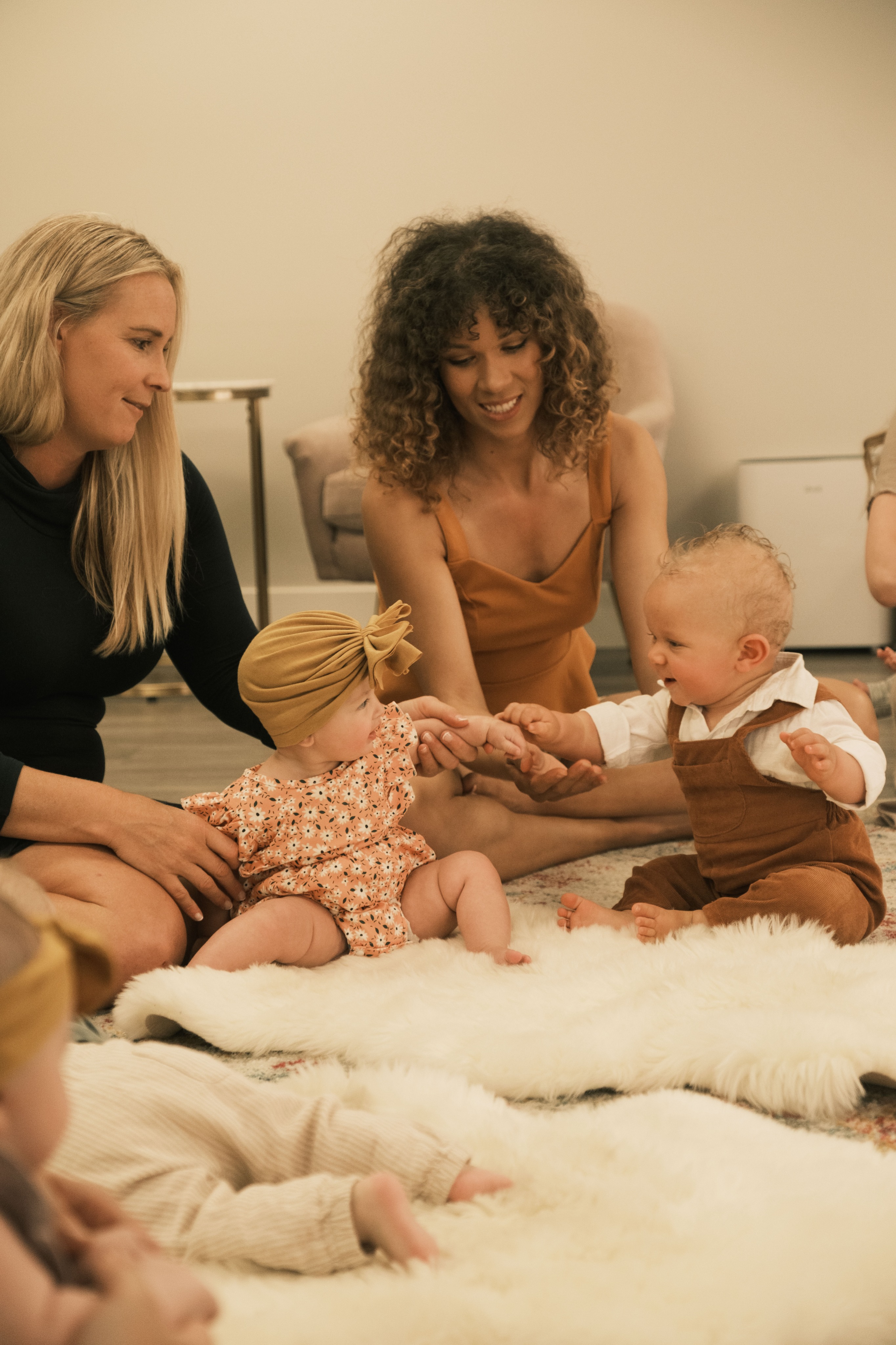 Two babies play together with their moms' support