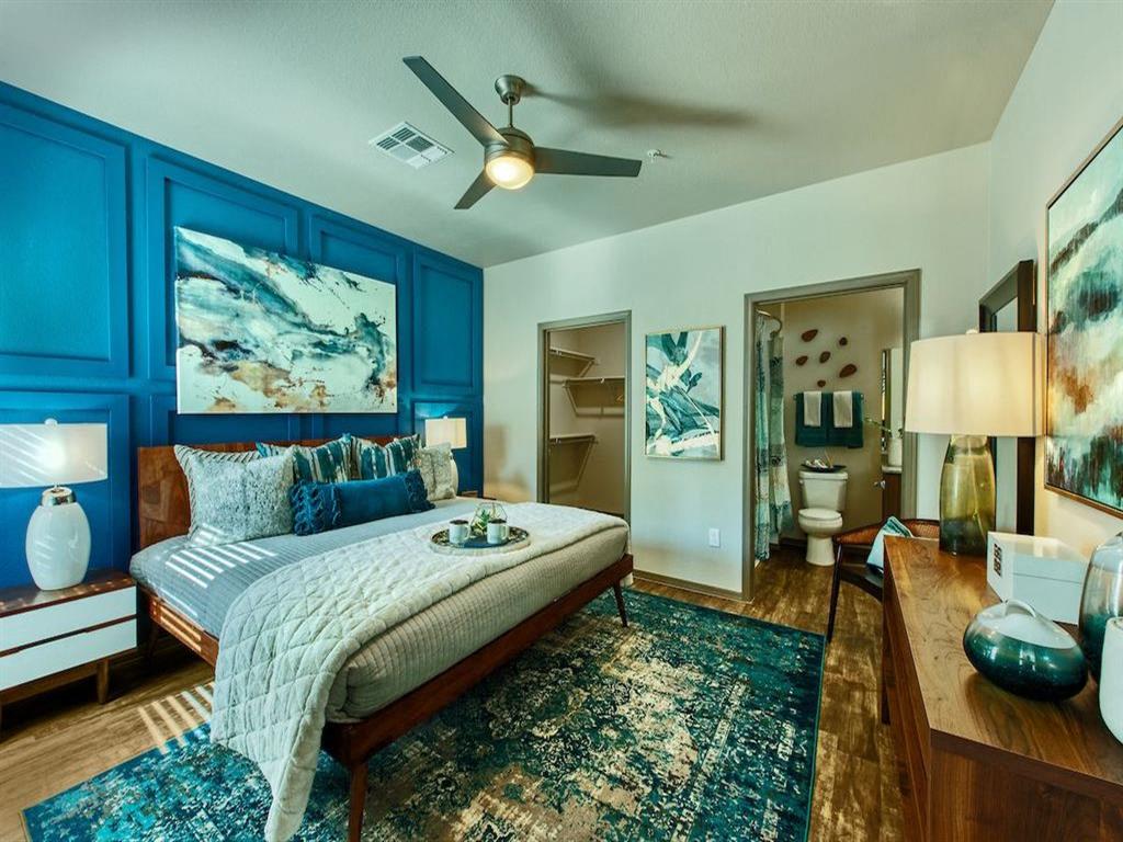 A bedroom with queen size bed and blue accent colored wall behind it. A door leads to the a bathroom and a second door shows the walk-in closet.