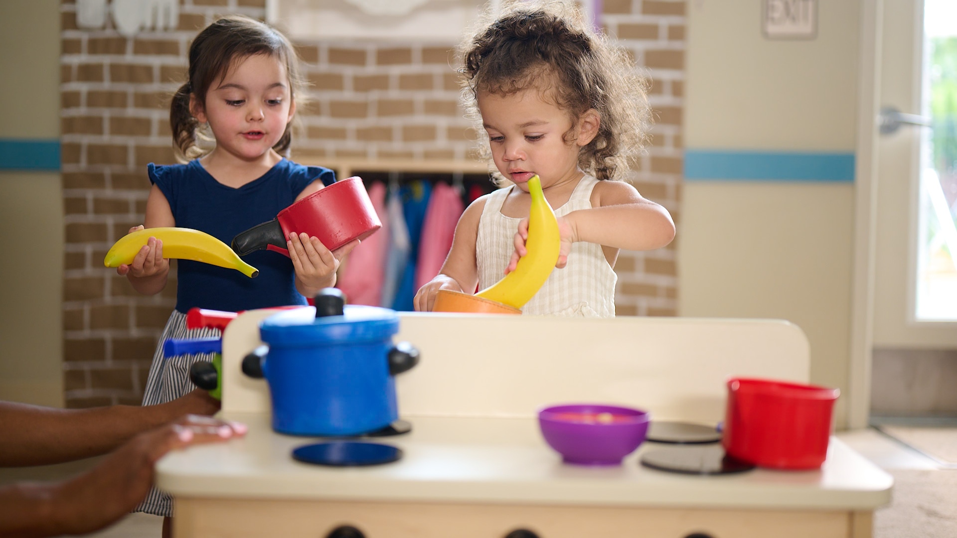 Two Primrose Schools toddlers engaged in imaginative dramatic play at toy kitchen in early learning classroom