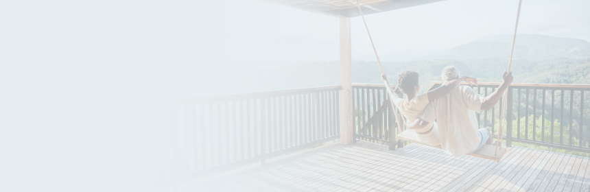 A mature couple on a patio swing looking out over a forest.