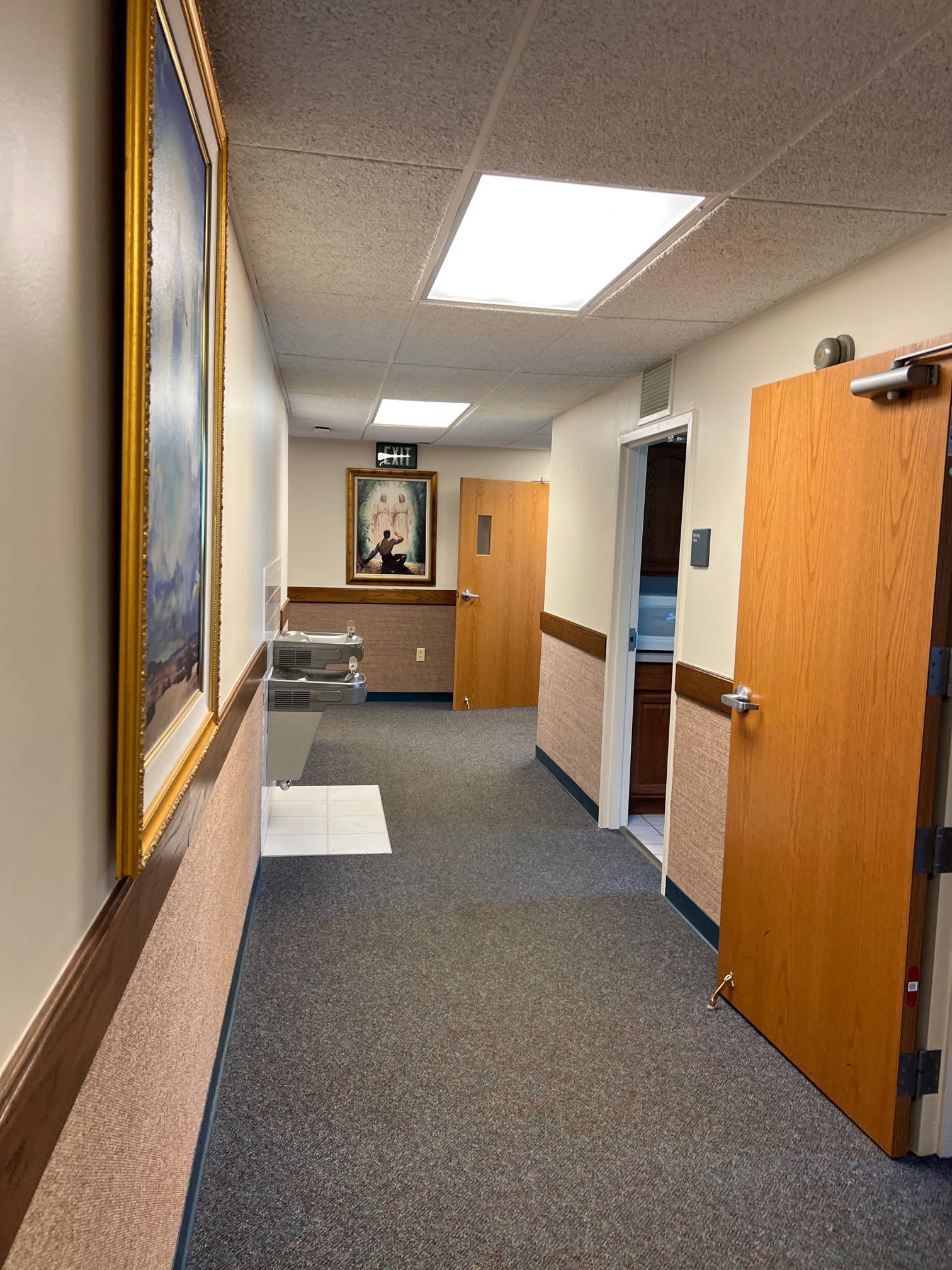 Hallway inside the church at 1155 Michigan Road in Madison, Indiana, with a painting of Joseph Smith's First Vision in focus.  Joseph is kneeling looking up at the Father and the Son.