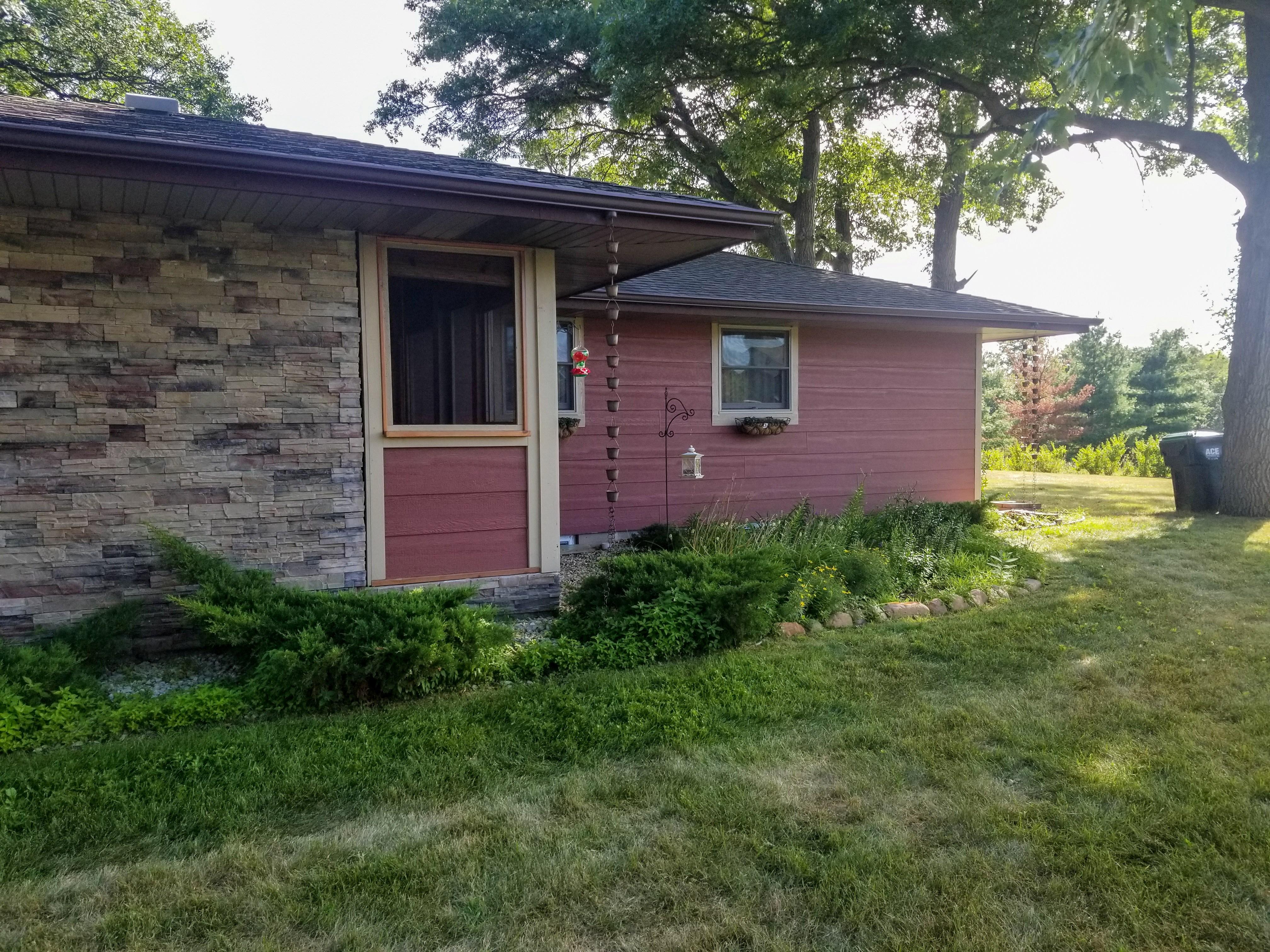 Dark brown seamless gutters featuring multiple decorative rain chains installed on a stone and red wood siding home by Ultimate Gutter Solutions.