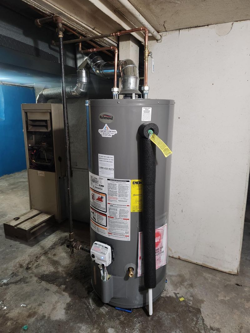 A grey Richmond brand gas water heater is professionally installed in a basement, featuring copper piping, a silver exhaust vent, and foam insulation on the temperature and pressure relief valve.