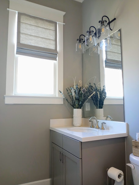 We can help make a statement in any room with our fabric Roman Shades. This elegant window covering brings in the light as well as design to this small bathroom.