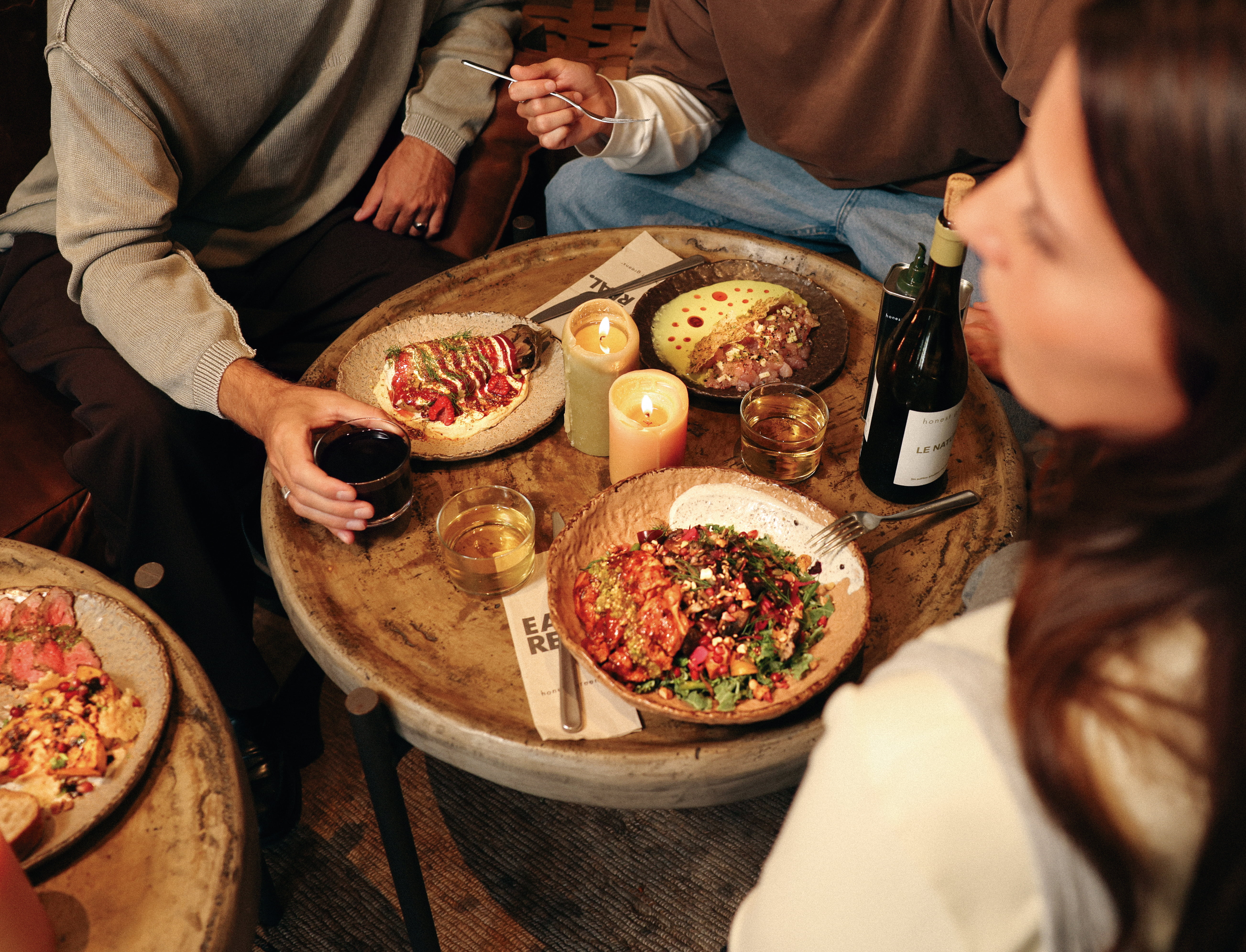 Friends around a candlelit table with autumn dishes and drinks.