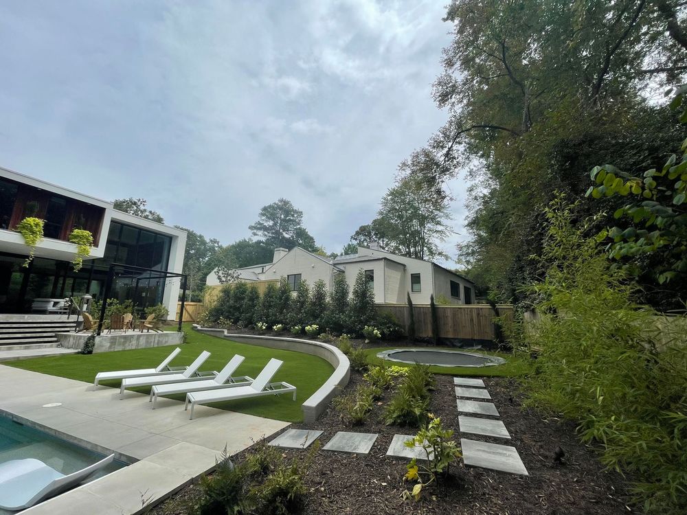 This upscale outdoor living space showcases contemporary design with a clean-lined pool area, manicured lawn, and tiered garden beds. Integrated recreational features like a sunken trampoline complement the modern architecture.