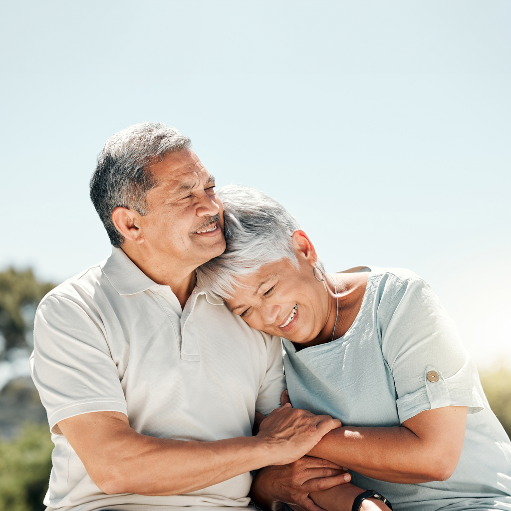 An elderly couple embracing outside.