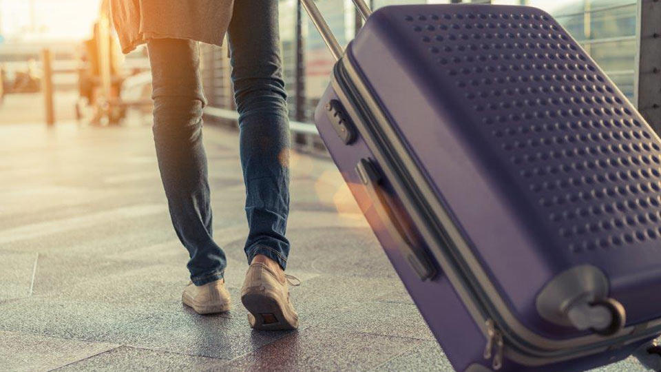 A traveler confidently strides down the airport terminal rolling her luggage behind her