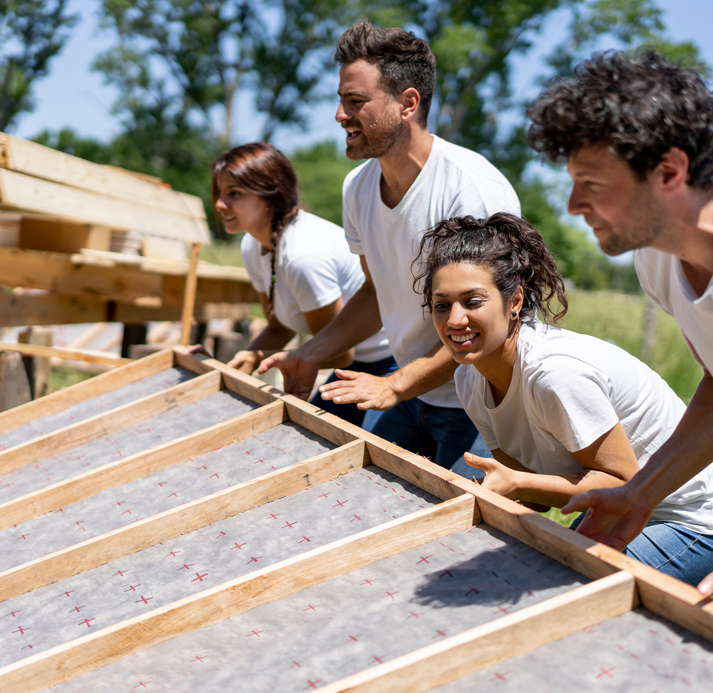 Four young adults volunteering together and building a structure on a sunny day.