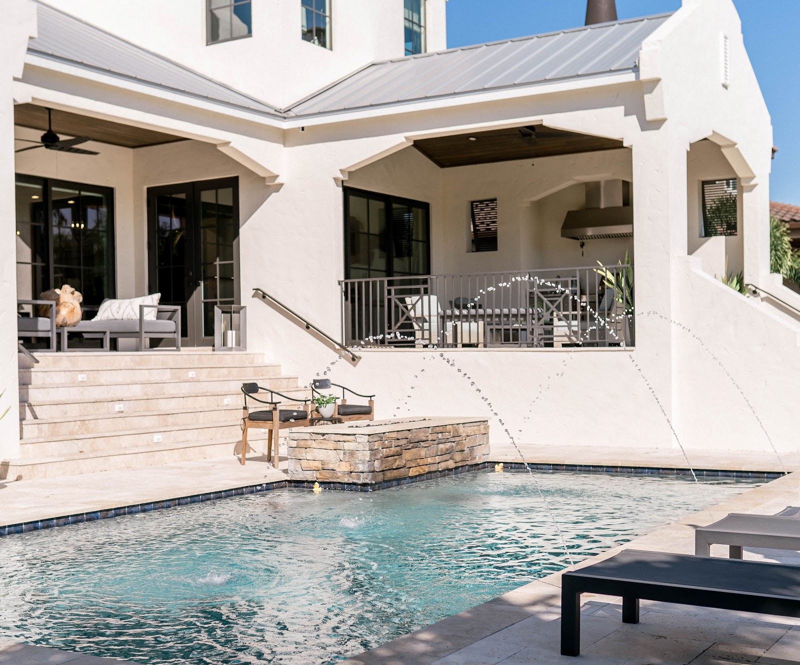 Luxury backyard swimming pool beside a modern home with stone steps, a covered patio, and elegant outdoor seating.