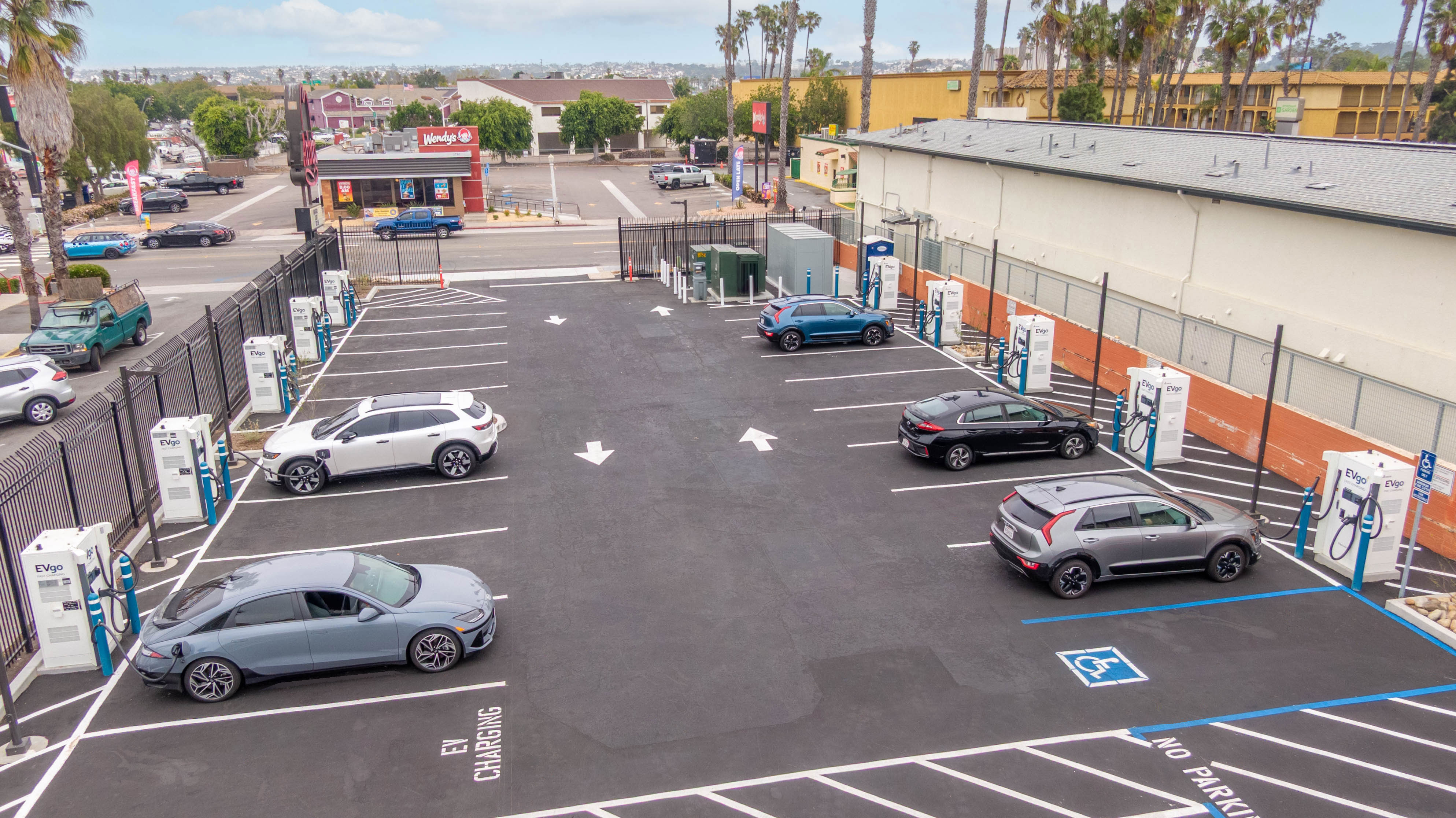 aerial photo of evgo charging station. multiple cars parked at station charging simultaneously in a large open ev charging lot.