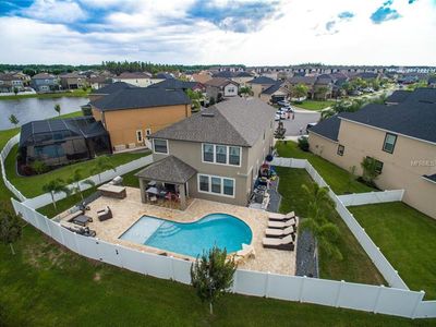 Aerial view of a suburban home with a backyard swimming pool, patio area, white privacy fence, and surrounding neighborhood.