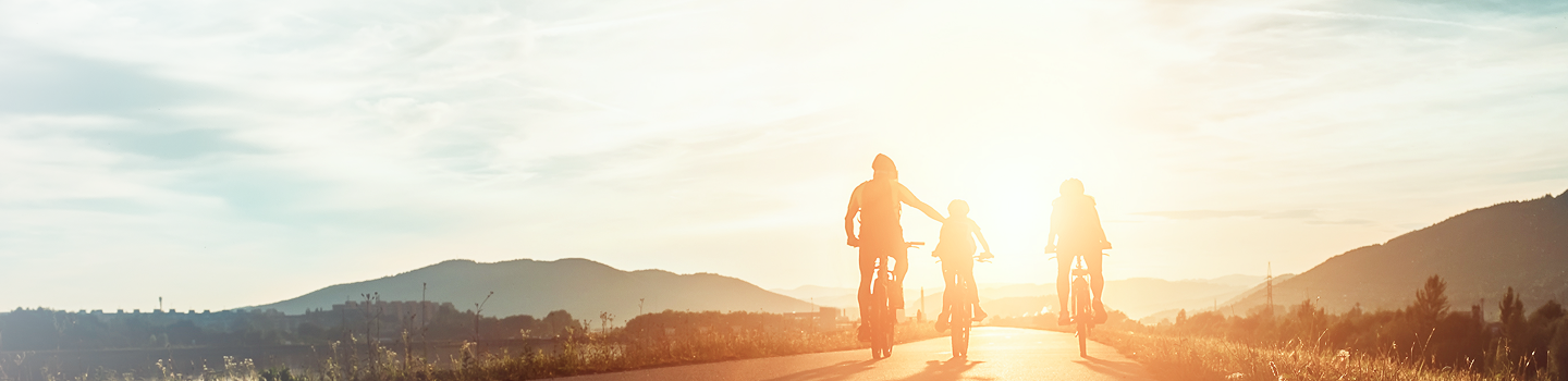 A family of three cycling together towards the sunset.