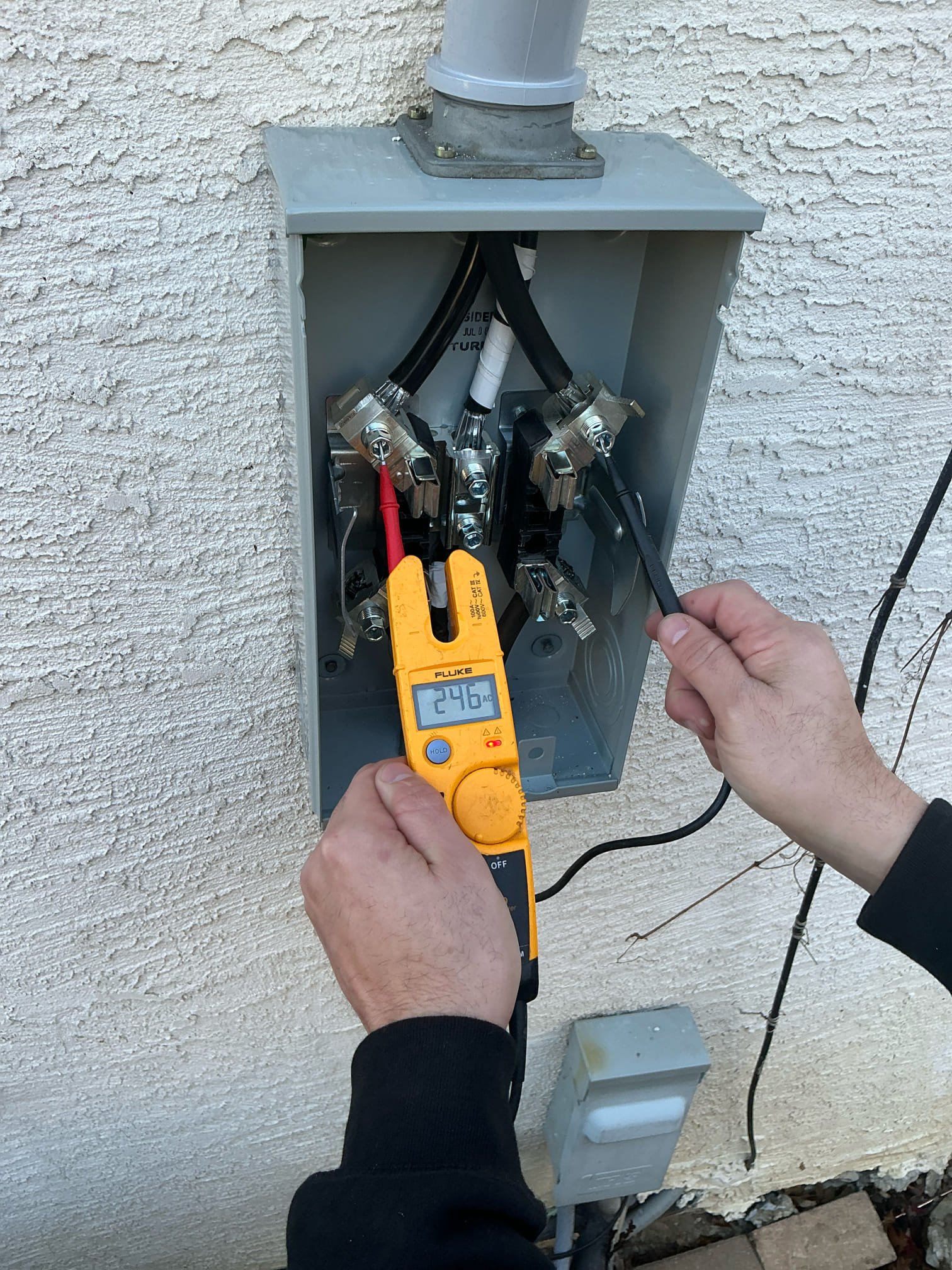 A Thomas Edison Electric technician uses a Fluke T5 electrical tester to verify 246 volts AC at an exterior meter base in Bryn Mawr, PA. Confirming proper voltage at the service entrance is a critical step during panel upgrades and electrical inspections.