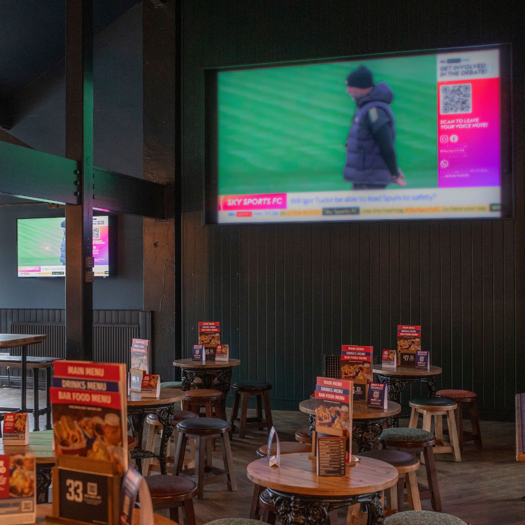 Seating area at The Arrow featuring tables, chairs and large TV screen, great space to watch live sports.