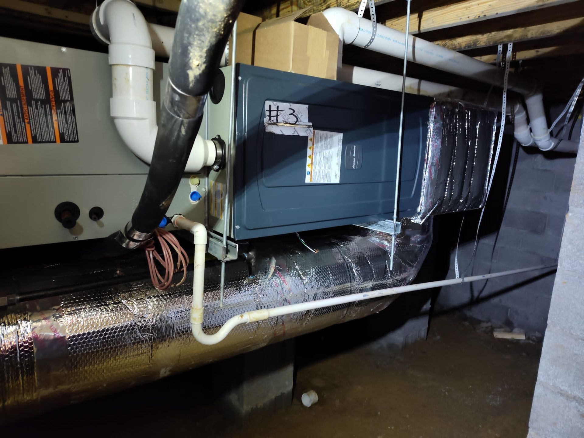Crawlspace HVAC air handler connected to insulated ductwork and white PVC drain piping, suspended be 