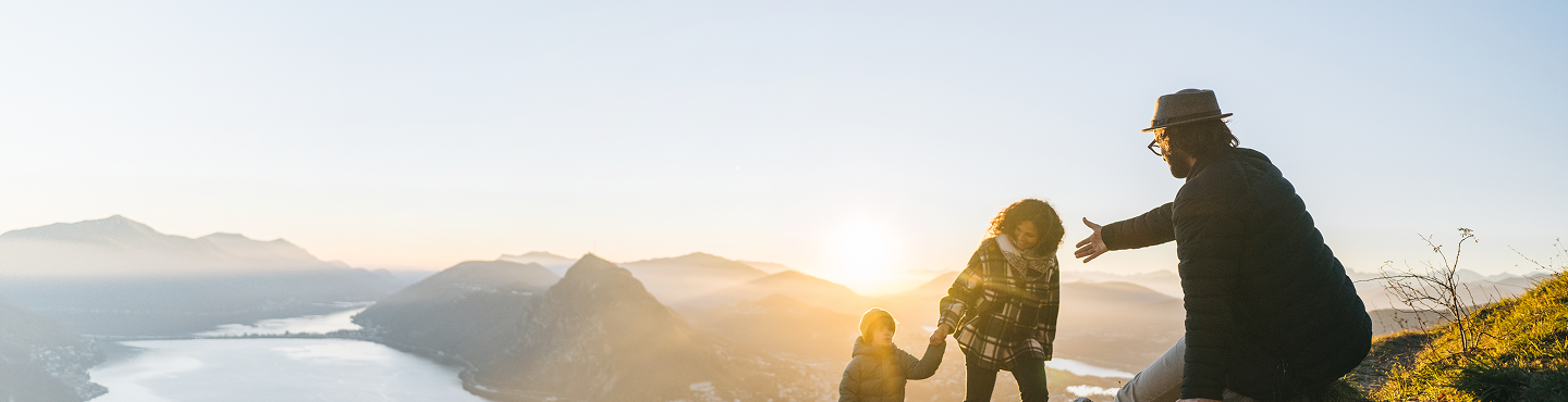 Une famille gravissant une montagne ensemble, avec une vue magnifique en arrière-plan.