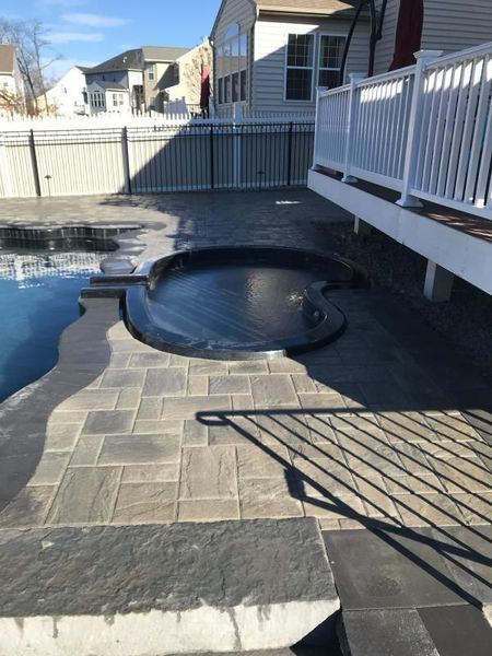 Backyard patio with installed hot tub and surrounding paver surface near residential deck. The layout demonstrates precision hardscaping work, integrating relaxation features with durable materials, enhancing outdoor usability and overall property value through professional installation.